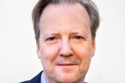 Portrait von Tom Krebs. Er trägt ein hellblaues Hemd sowie einen dunkelblauen Blazer.