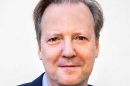 Portrait von Tom Krebs. Er trägt ein hellblaues Hemd sowie einen dunkelblauen Blazer.