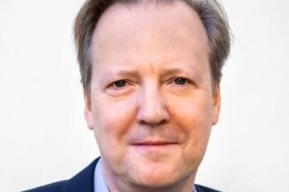 Portrait von Tom Krebs. Er trägt ein hellblaues Hemd sowie einen dunkelblauen Blazer.