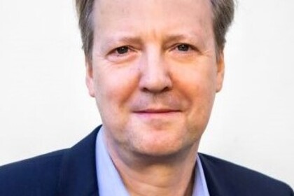 Portrait von Tom Krebs. Er trägt ein hellblaues Hemd sowie einen dunkelblauen Blazer.