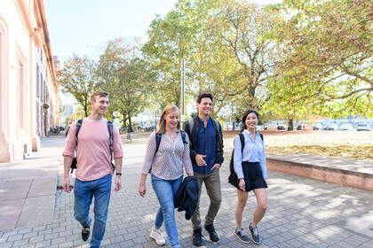 Four students are walking on a path in front of the castle, laughing