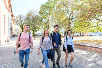 Vier Studierende laufen lachend auf einem Weg vor dem Schloss