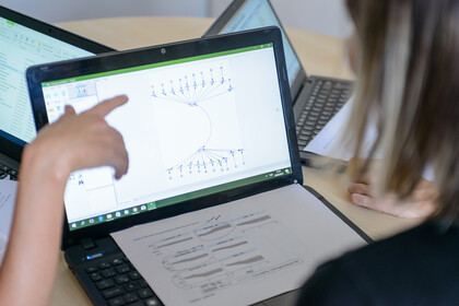 Auf einem Tisch stehen drei aufgeklappte Laptops. Eine Person zeigt auf einen Laptop auf welchem ein Graph zu sehen ist.
