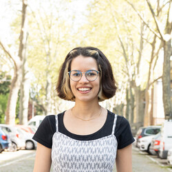 Eine Studentin in kurzem Kleid läuft lachend über eine verkehrsberuhigte Straße mit Kopfsteinpflaster