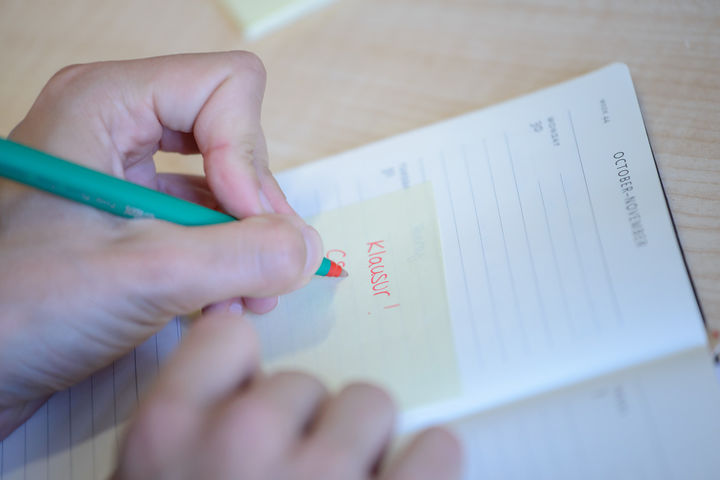 Eine Hand schreibt mit rotem Stift "Klausur!" in einen Kalender 
