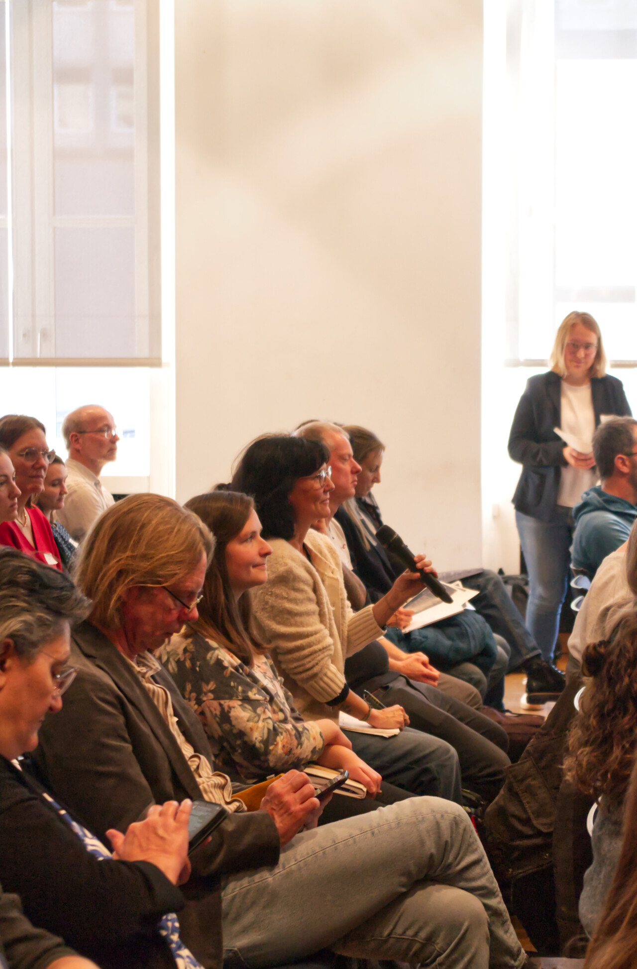 Blick ins Publikum, eine Teilnehmerin stellt ihre Diskussionfrage in ein Mikrofon.