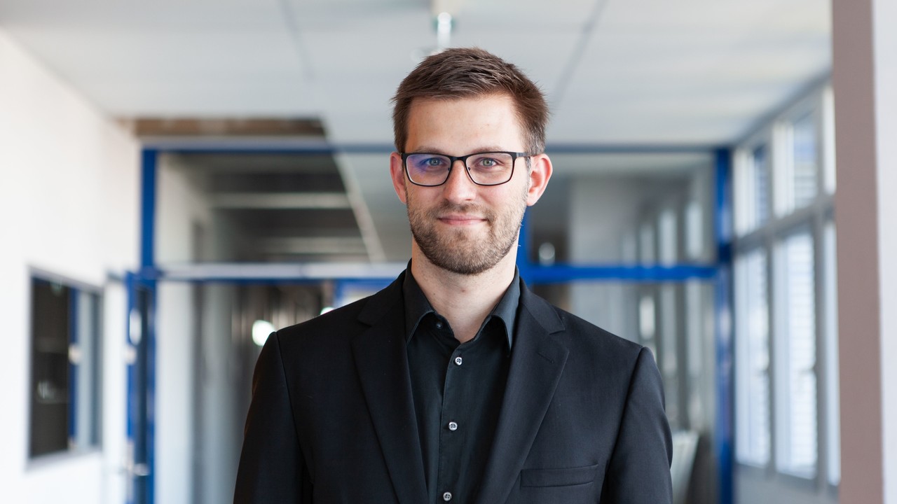 Dr. Stefan Janke hat kurze braune Haare, einen Bart und eine Brille. Er trägt ein schwarzes Jacket und ein schwarzes Hemd.