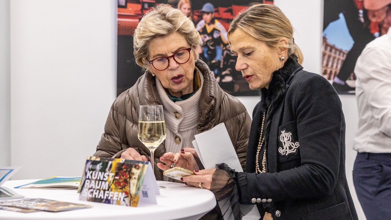 Zwei weiblich gelesene Personen stehen vor einem Stehtisch bei der Spitzensport-Vernissage.