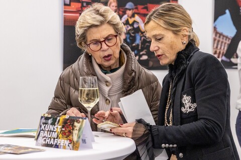 Zwei weiblich gelesene Personen stehen vor einem Stehtisch bei der Spitzensport-Vernissage. 