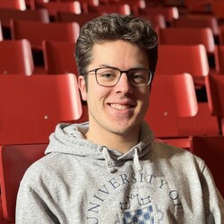 Portät von Magnus Dröse. Magnus Dröse trägt eine Brille und einen grauen Kapuzenpullover mit dem Logo der Uni Mannheim. Seine Haare sind kurzgeschnitten und dunkelblond.