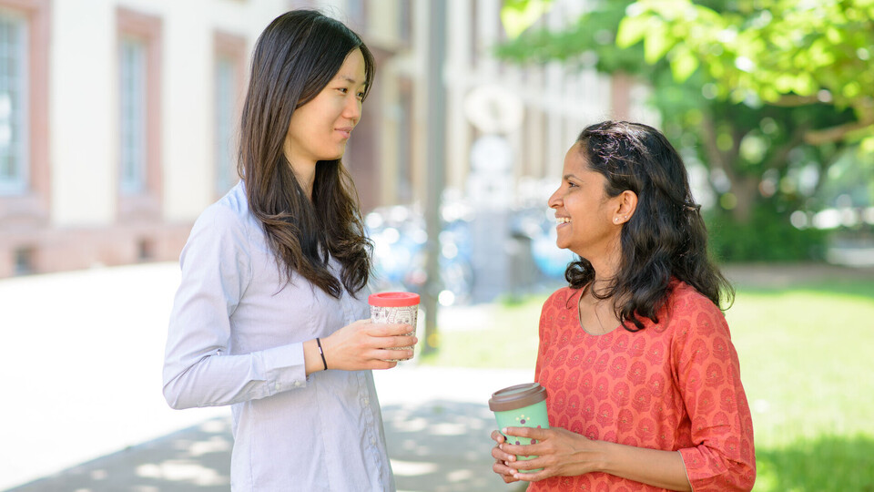 Internationale Forschende Zwei Frauen mit Kaffebechern unterhalten sich.