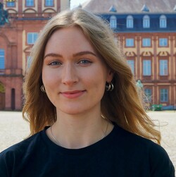 Eva Bretschneider is wearing a black T-shirt and hoop earrings. She has blue eyes and rather long blond hair, which is worn loose.