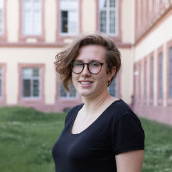 Hannah Merzhäuser steht lächelnd auf der Mensawiese. Im Hintergrund das Schloss.