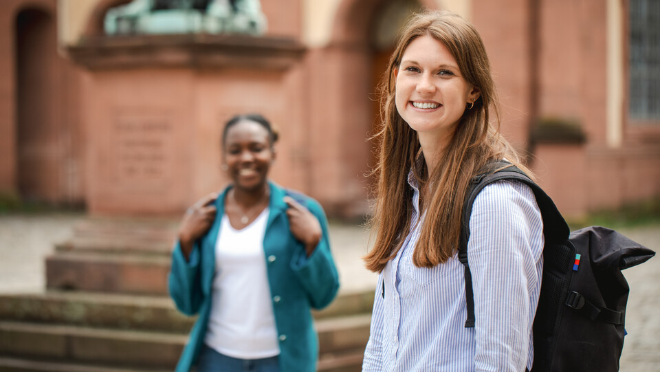 Zwei Frauen stehen auf dem Ehrenhof der Uni Mannheim und lachen.