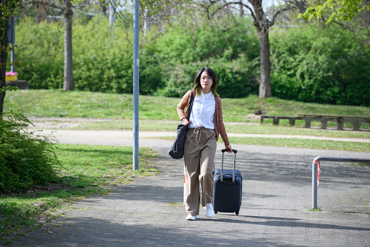 A doctoral student is walking on a street with a suitcase.