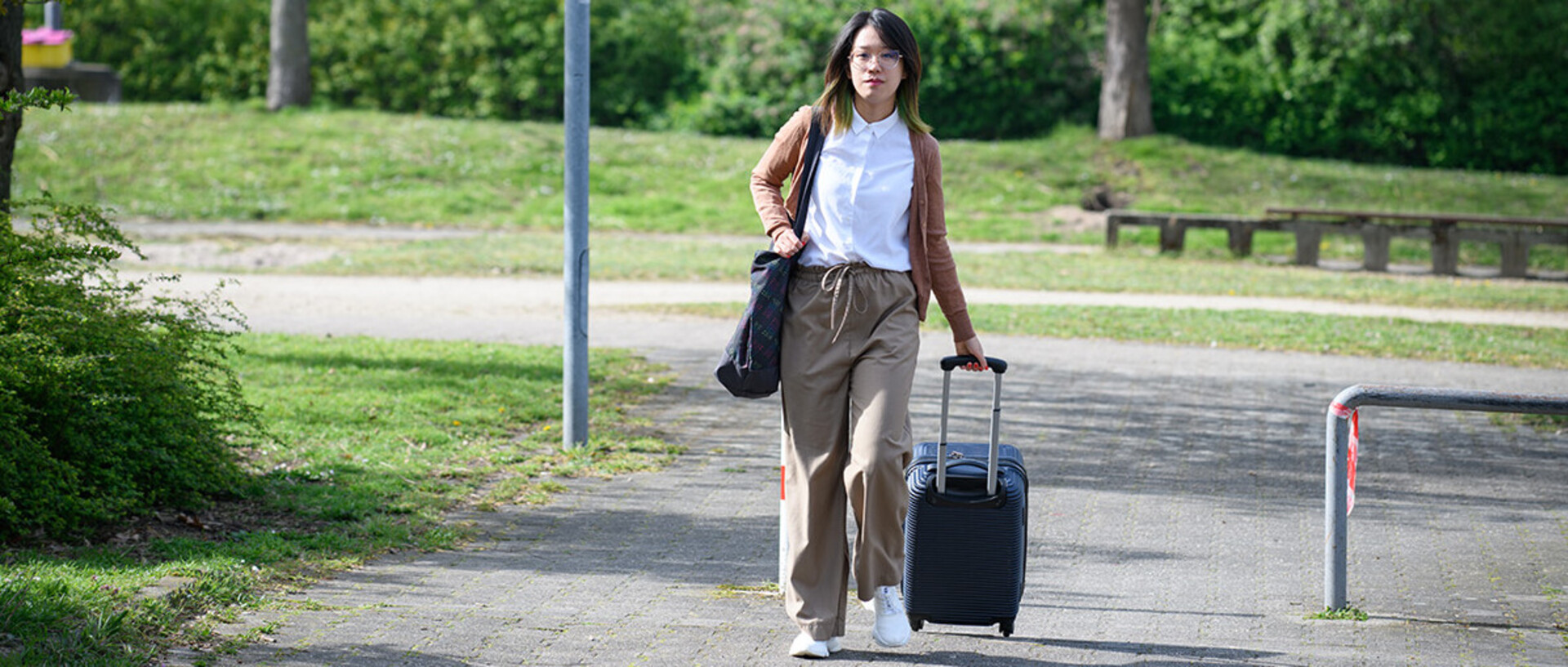 A doctoral student is walking on a street with a suitcase.