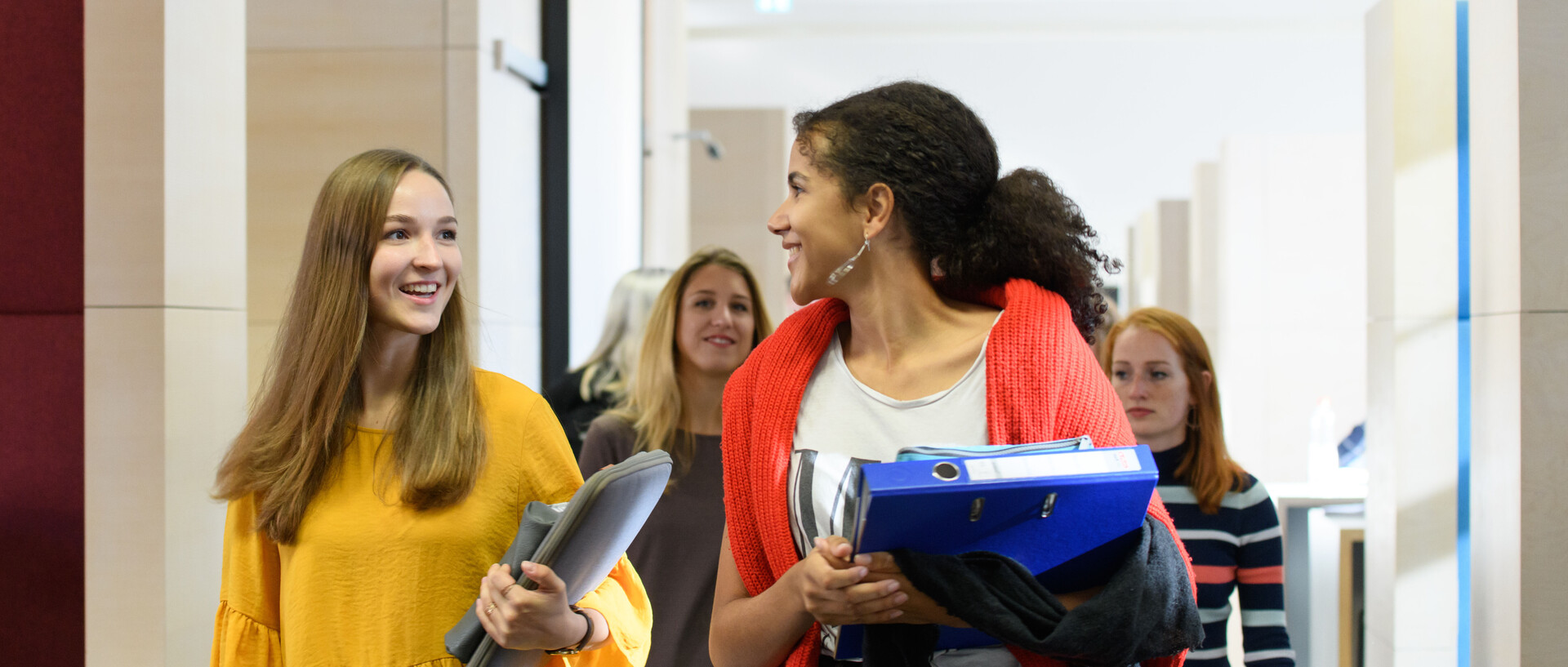 Studentinnen der Uni Mannheim laufen lachend und sich unterhaltend über einen Flur
