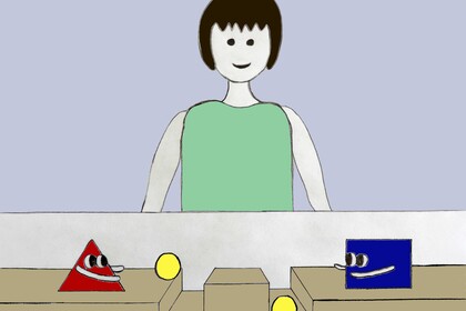 Eine Figur steht hinter einem Karton. Auf dem Karton stehen links ein rotes Dreieck und rechts ein blaues Rechteck mit Augen und Armen. Die Formen werfen gelbe Bälle in zwei Rillen vor ihnen.