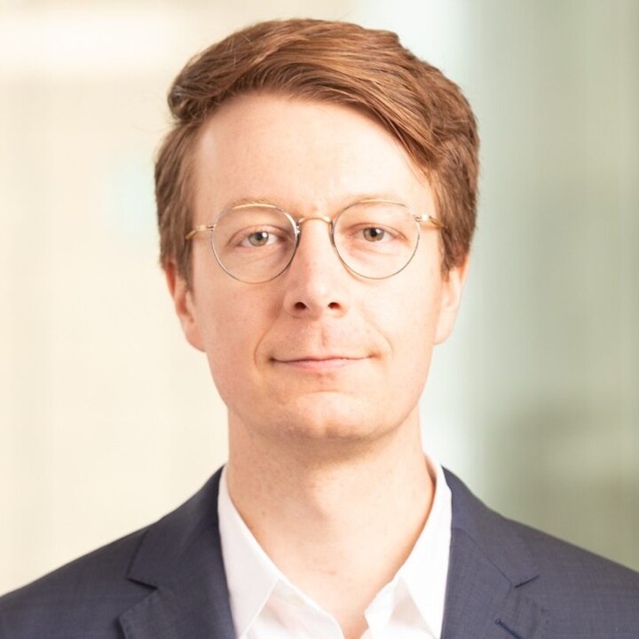 Florian Heeb hat kurze rötliche Haare. Er trägt eine runde Brille, ein weißes Hemd und einen schwarzen Blazer.