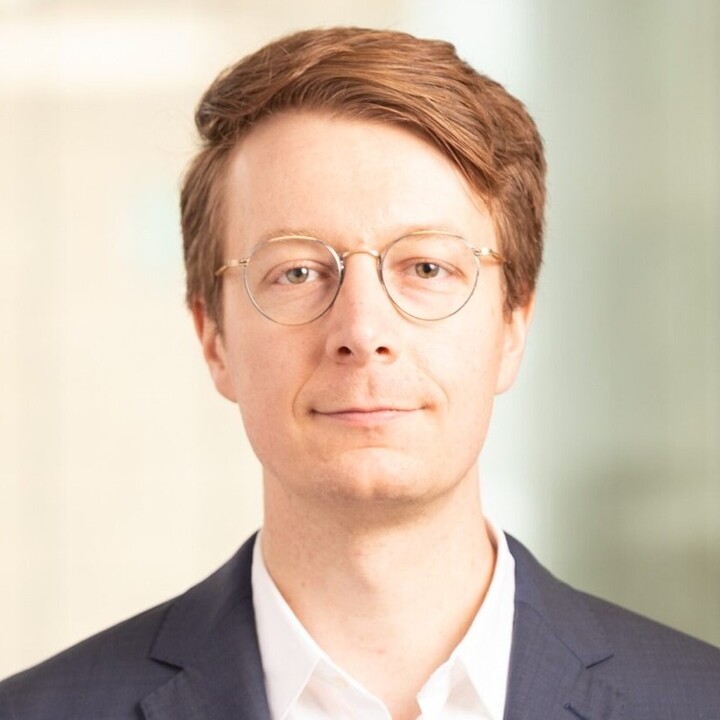 Florian Heeb hat kurze rötliche Haare. Er trägt eine runde Brille, ein weißes Hemd und einen schwarzen Blazer.