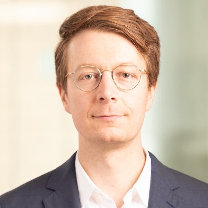 Florian Heeb hat kurze rötliche Haare. Er trägt eine runde Brille, ein weißes Hemd und einen schwarzen Blazer.