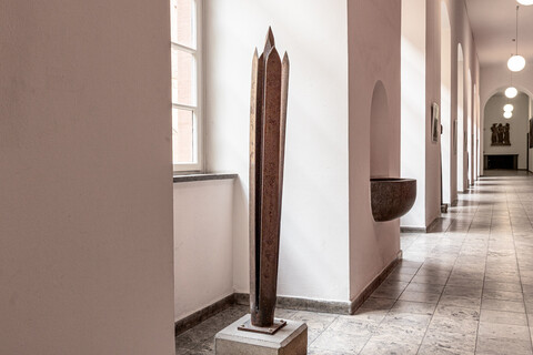 Skulptur im Rektoratsflur aus vier klingenförmigen Metallplatten mit einem längeren, spitzen Metallstück in der Mitte.