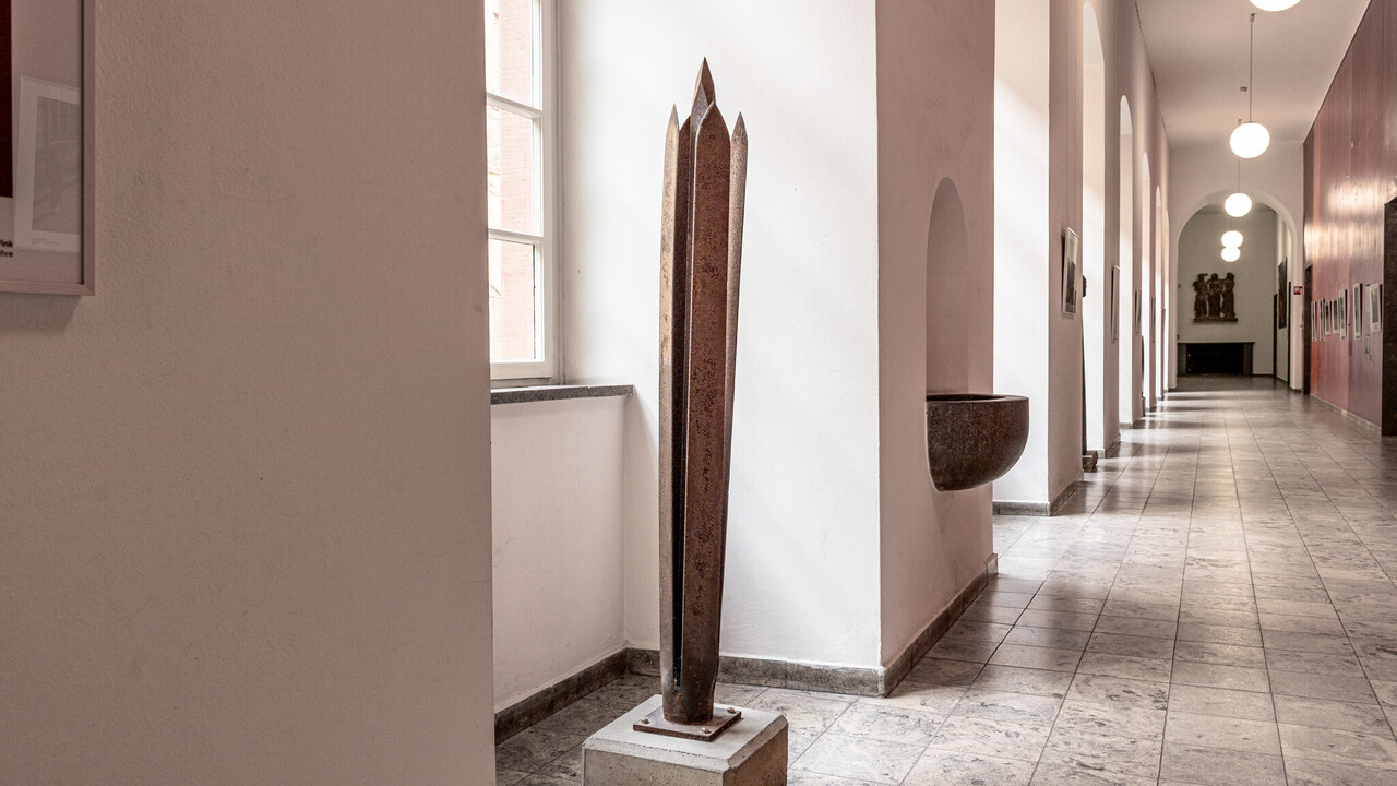 Skulptur im Rektoratsflur aus vier klingenförmigen Metallplatten mit einem längeren, spitzen Metallstück in der Mitte.