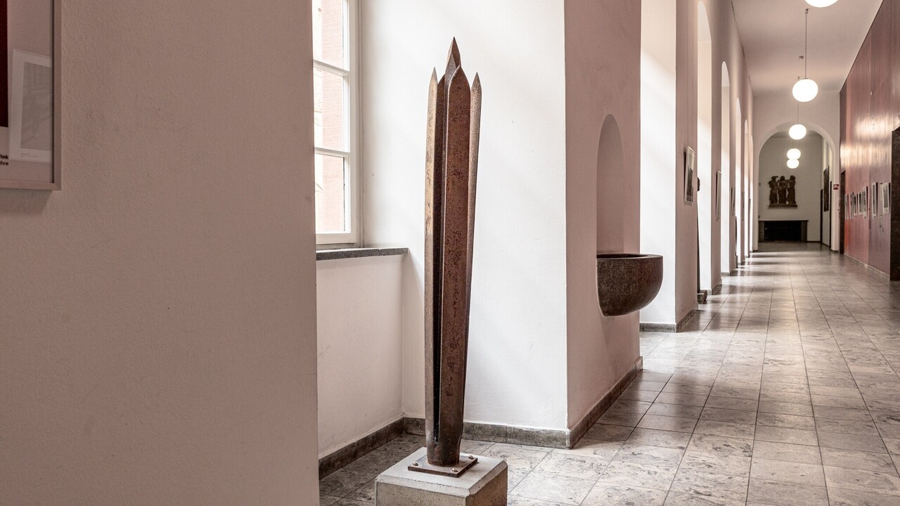 Skulptur im Rektoratsflur aus vier klingenförmigen Metallplatten mit einem längeren, spitzen Metallstück in der Mitte.