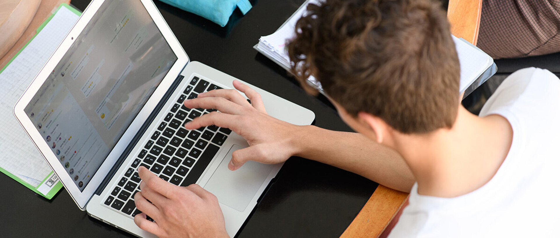 A student sits at a table and writes on his laptop.