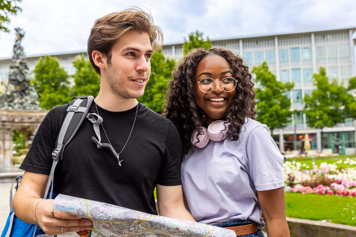 Ein Student und eine Studentin stehe im Freien. Der Student hat einen Plan in der Hand.