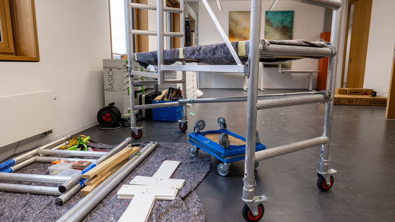 Man sieht ein fahrbares Gerüst. Auf dem Boden liegt ein Fließ. auf ihm liegen Einzelteile von Möbeln und Werkzeuge