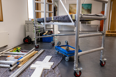 Man sieht ein fahrbares Gerüst. Auf dem Boden liegt ein Fließ. auf ihm liegen Einzelteile von Möbeln und Werkzeuge