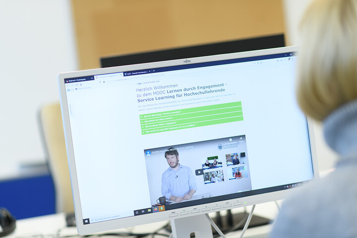 Eine Frau mit blonden Haaren sitzt vor einem Bildschirm. Auf dem Bildschirm ist eine Seite offen mit dem Titel "Herzlich Willkommen zu dem MOOC Lernen durch Engagement - Service-Learning für Hochschullehrende"
